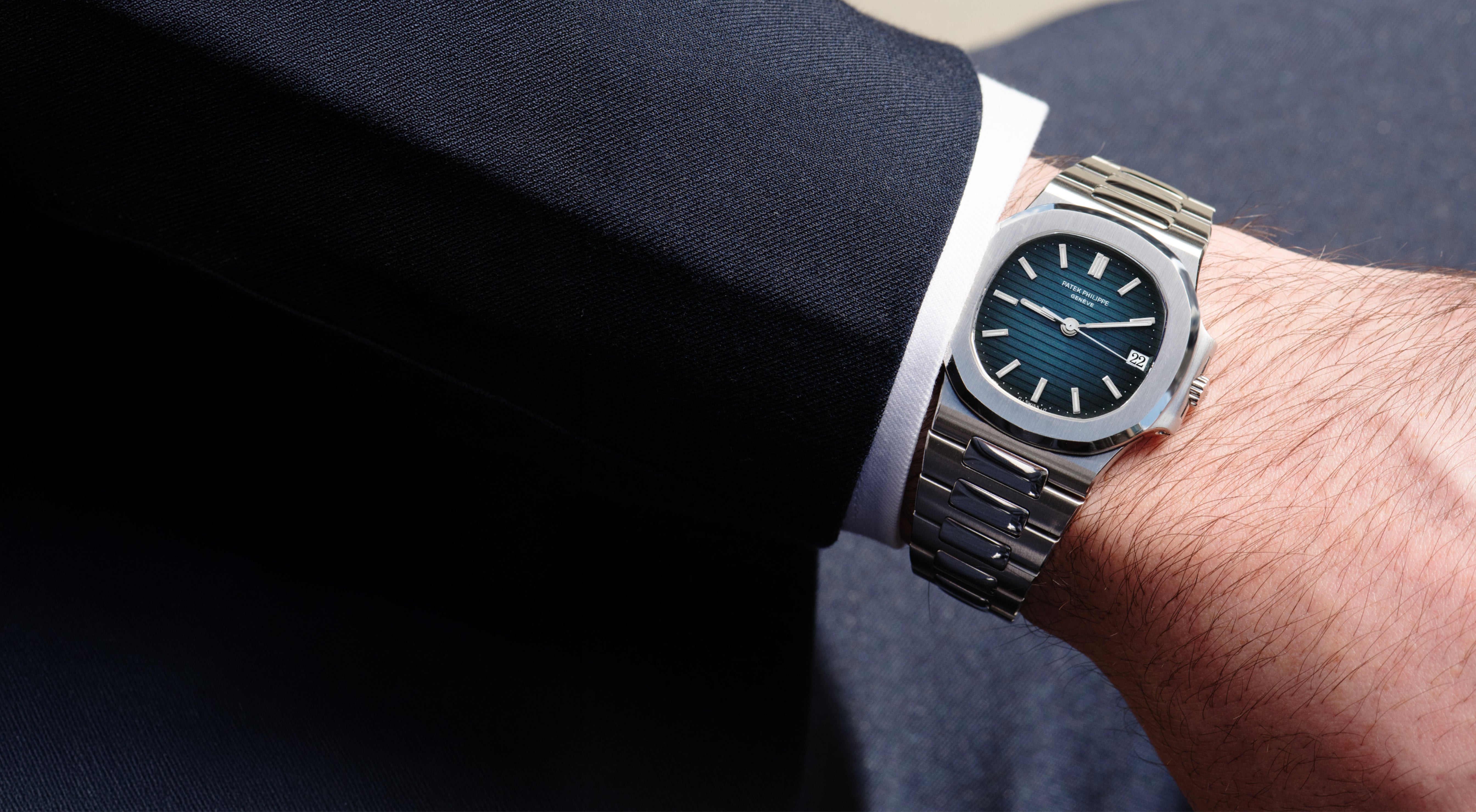Patek Philippe Nautilus 3800/1A in stainless steel worn with a dark suit, featuring a blue horizontally embossed dial, date display and integrated bracelet.